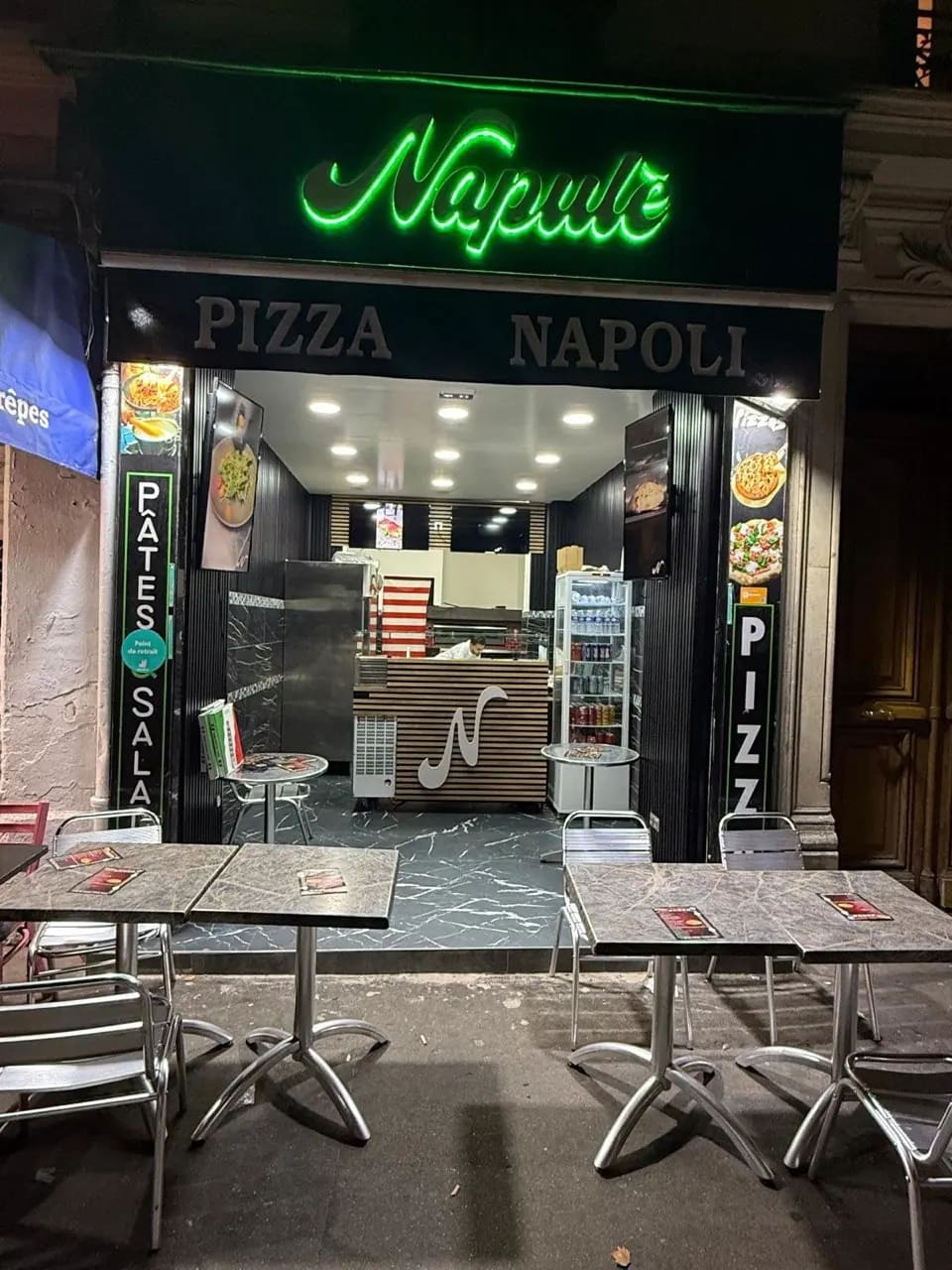 The front of L'art Napulè at night, green neon sign at 4 boulevard de Clichy in Paris, with pavement tables